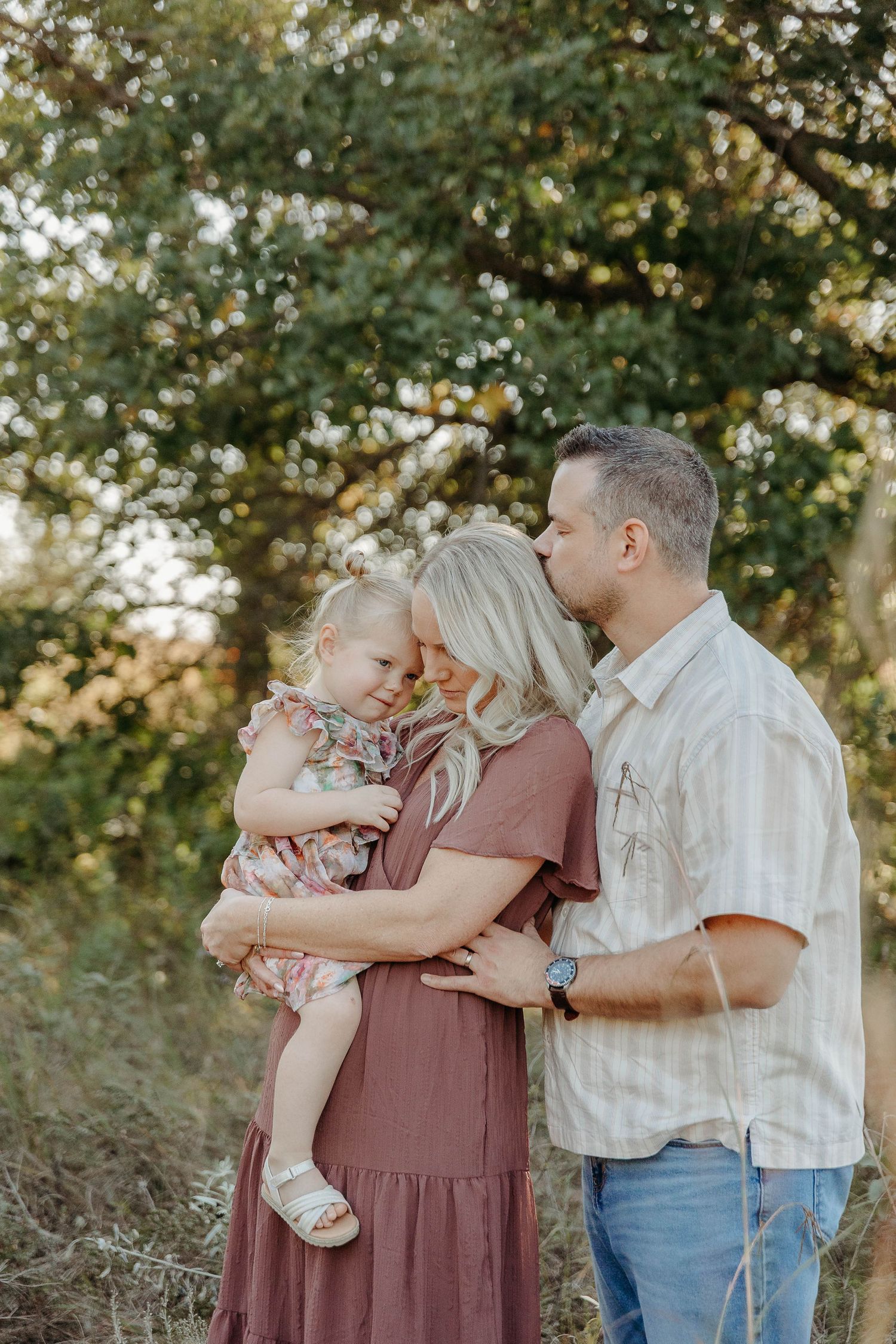 Family shares tender moments together outdoors during golden hour in a series of intimate portraits.