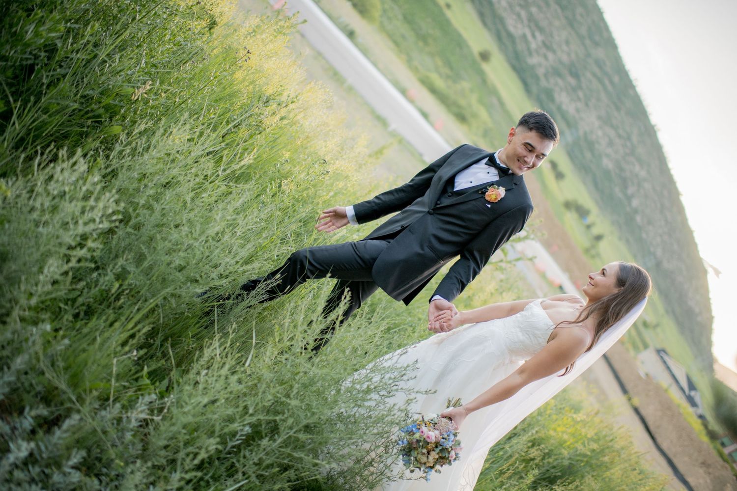 A couple in formal attire poses together in a grassy field during a summer photo session.