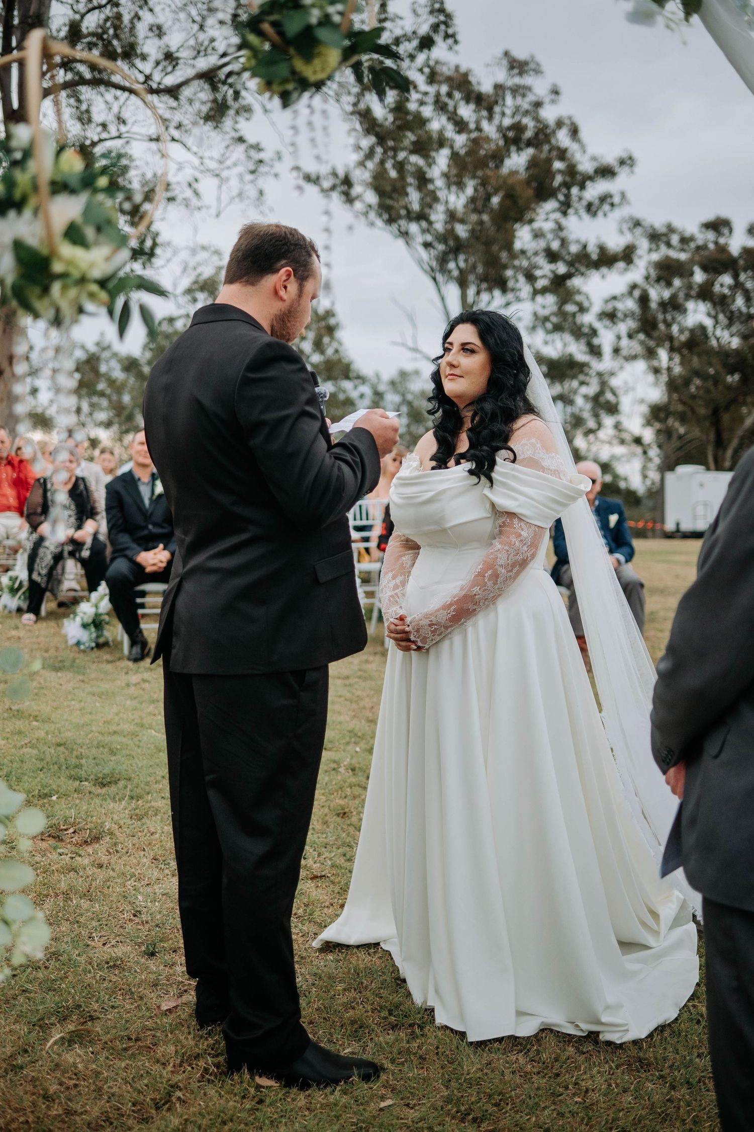 A romantic outdoor wedding ceremony kiss with guests cheering against a mountain backdrop.