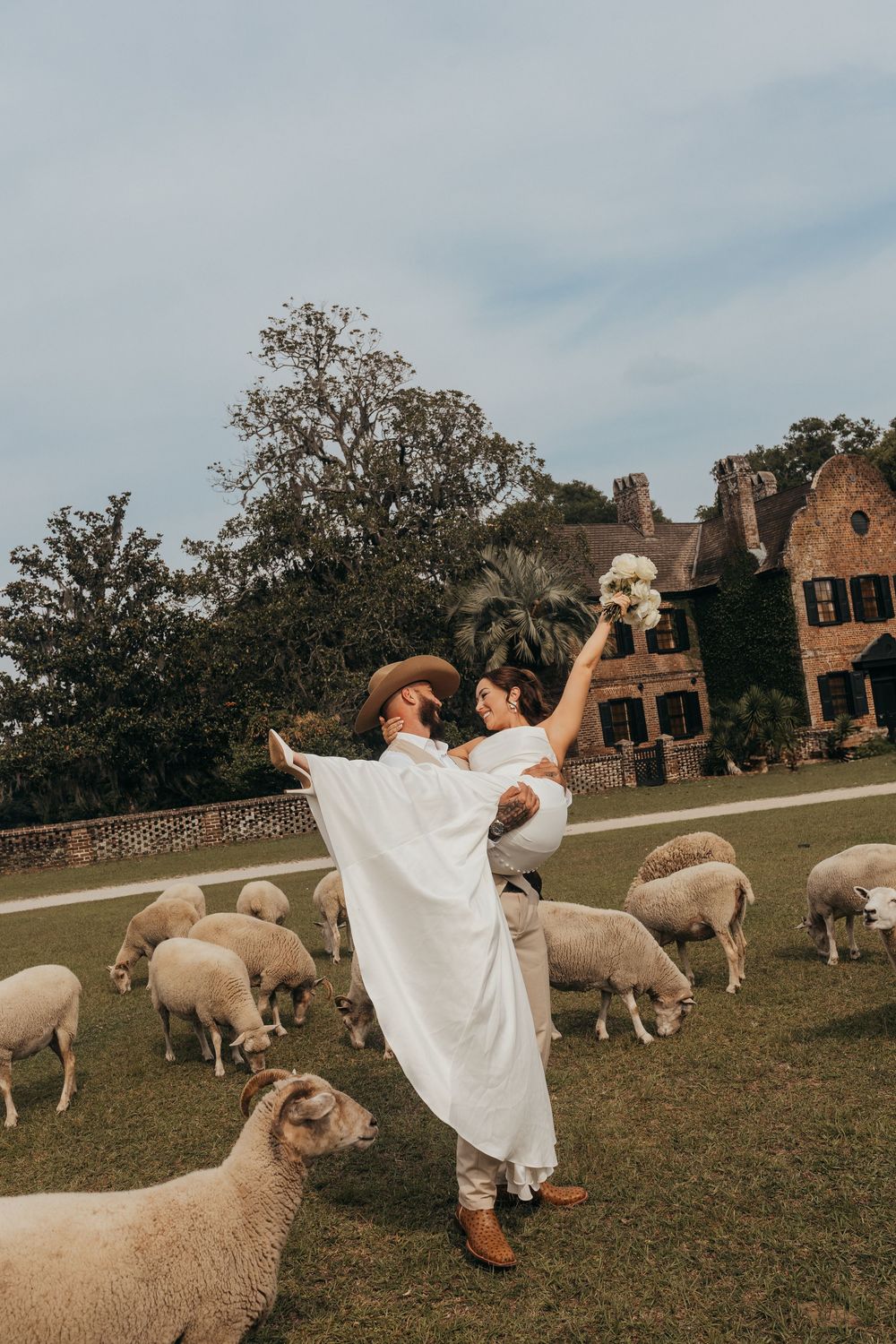 A figure in a white dress twirls and spins playfully in a field among grazing sheep with historic buildings in the background.