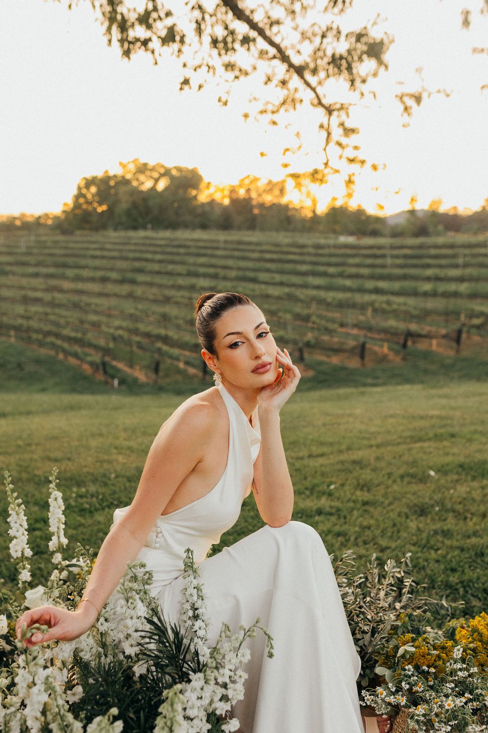 Elegant white dress photographed in front of vineyard rows at sunset with florals in foreground.