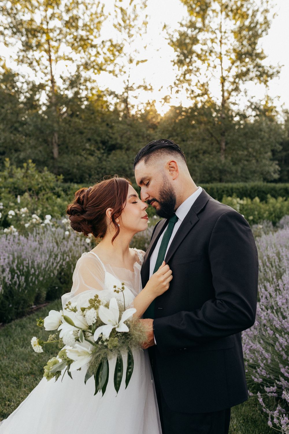 A romantic wedding couple embraces in a garden with lavender and white bouquet at sunset in the forest.