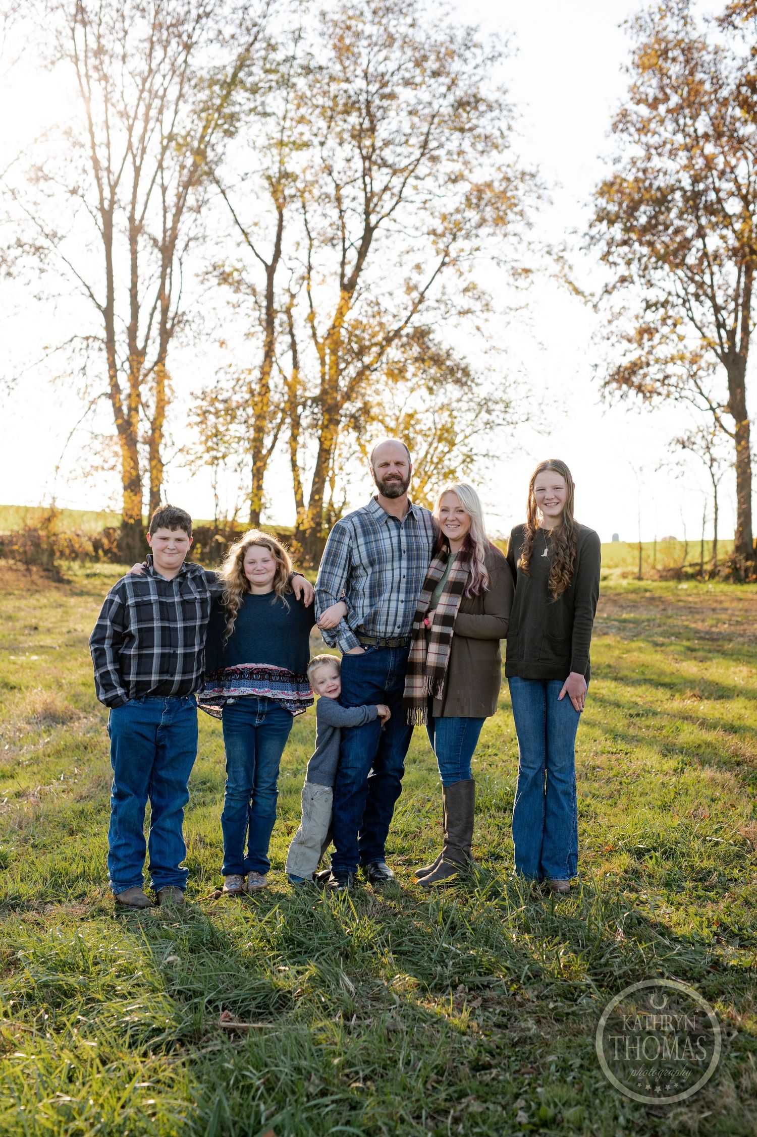 Family stands together in coordinated outfits during golden hour photo session.
