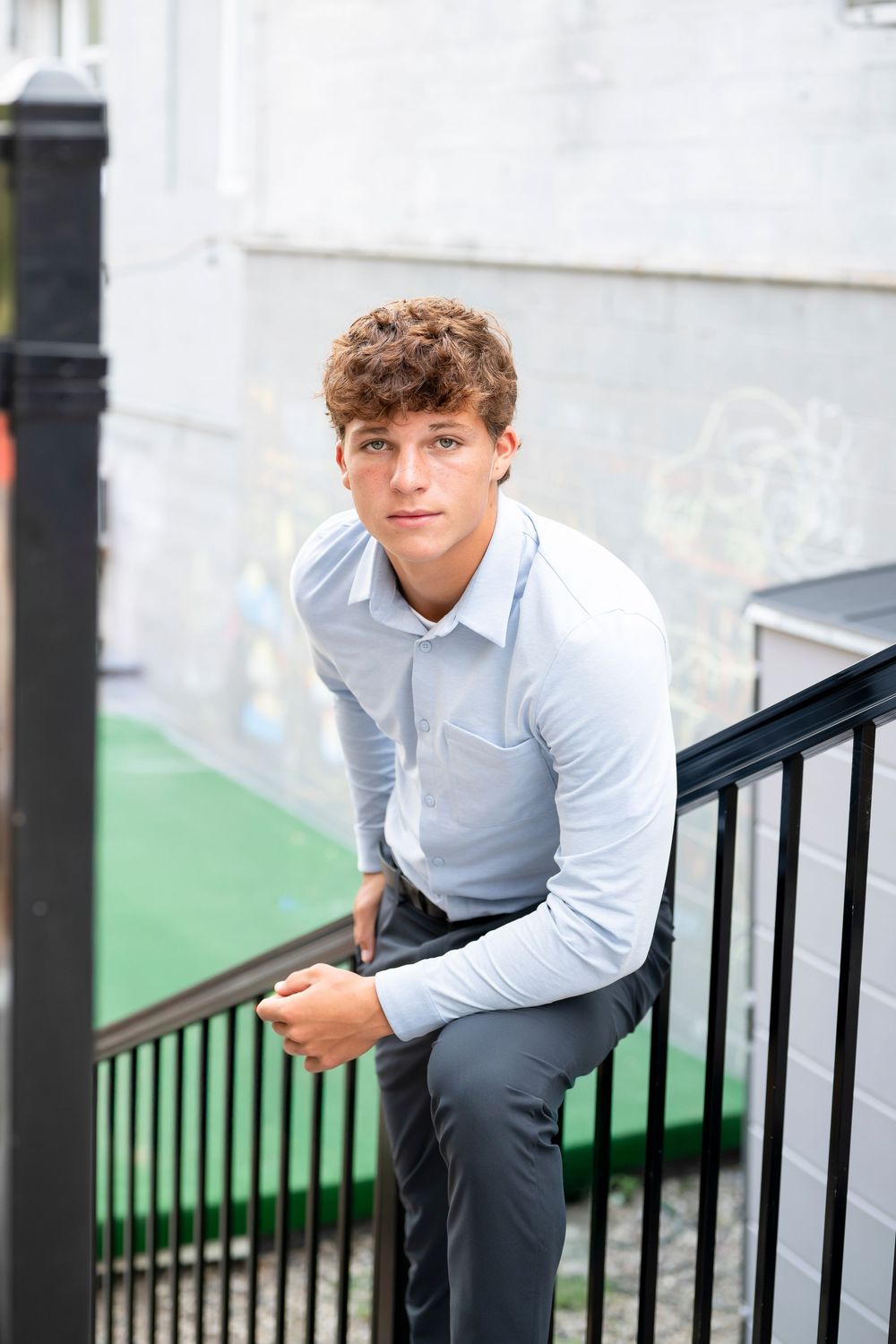 Young person in light blue shirt and dark pants poses on outdoor staircase.