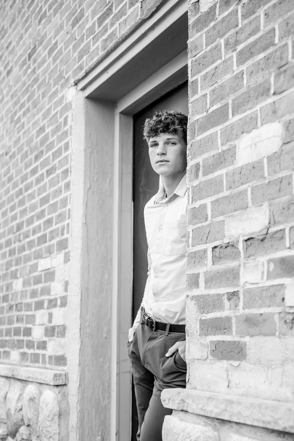Black and white portrait of student posing in doorway of brick building.