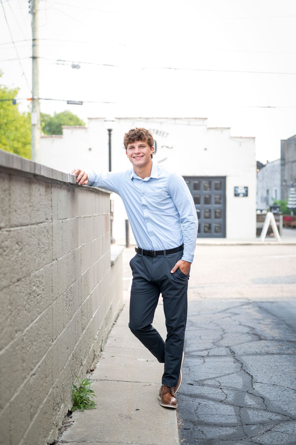 Student in business casual attire poses along concrete wall outdoors.