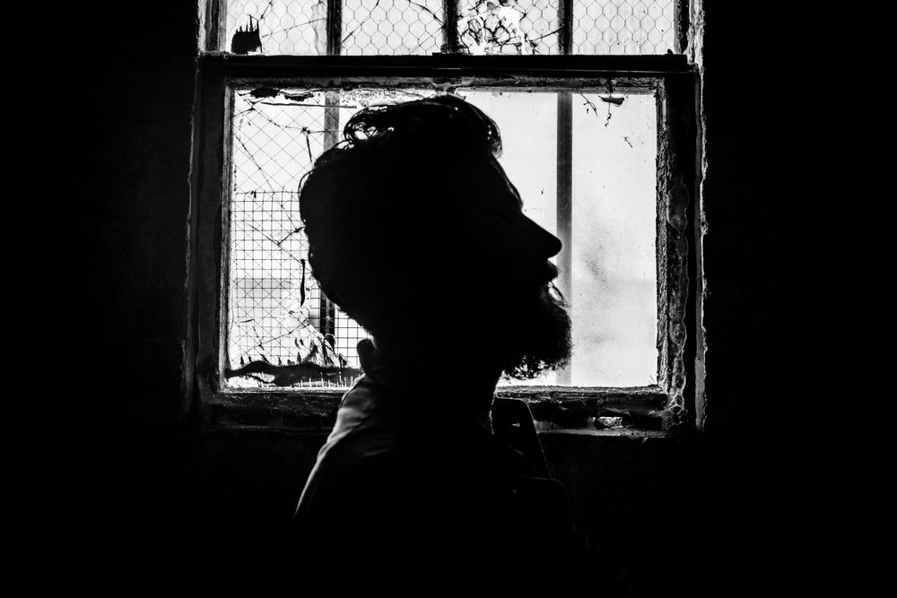 Silhouette portrait against window with textured glass creating dramatic contrast.