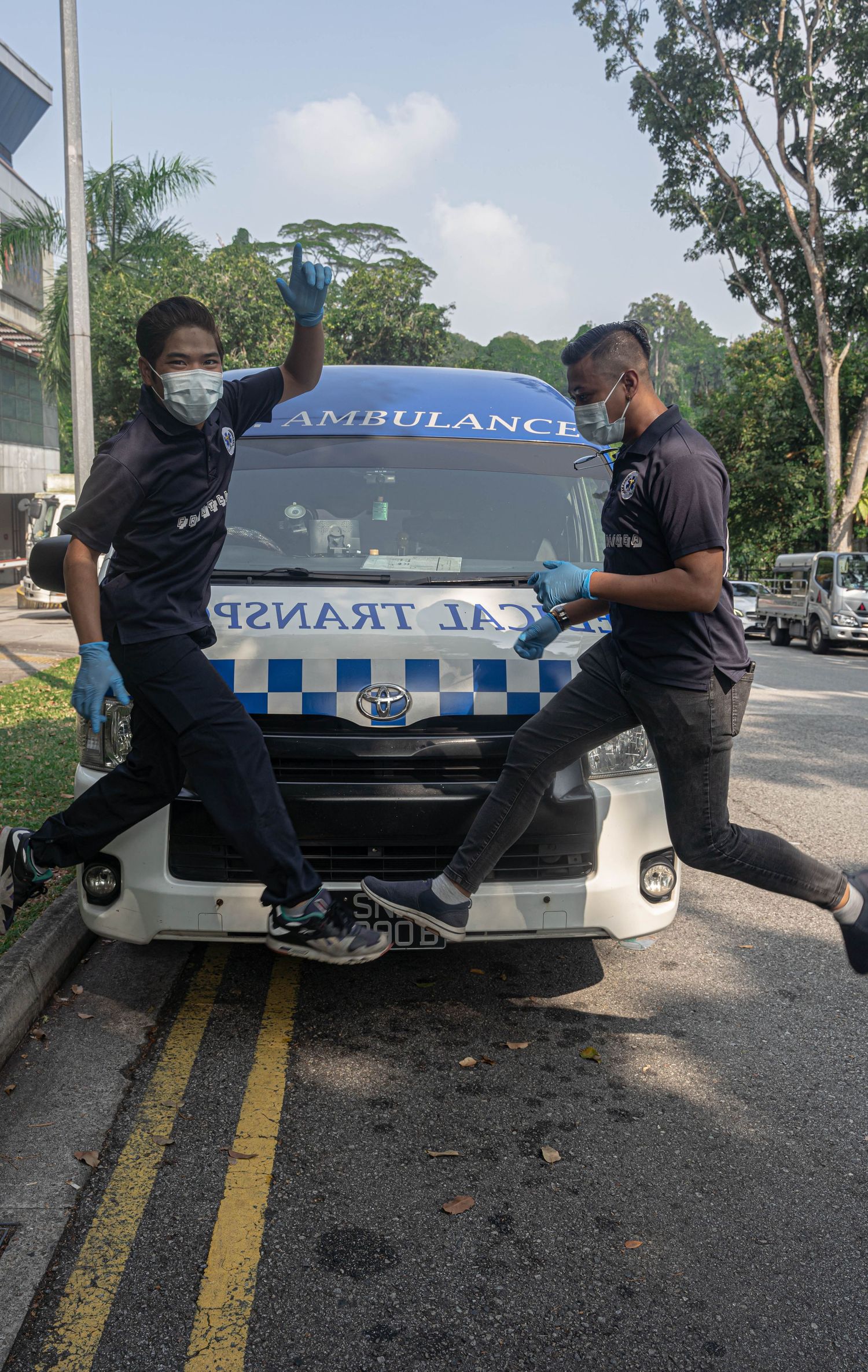Ambulance crew members in uniform posing playfully in front of their emergency vehicle.