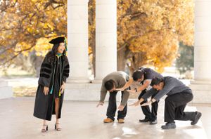 Group of friends in graduation attire playfully posing under autumn trees.