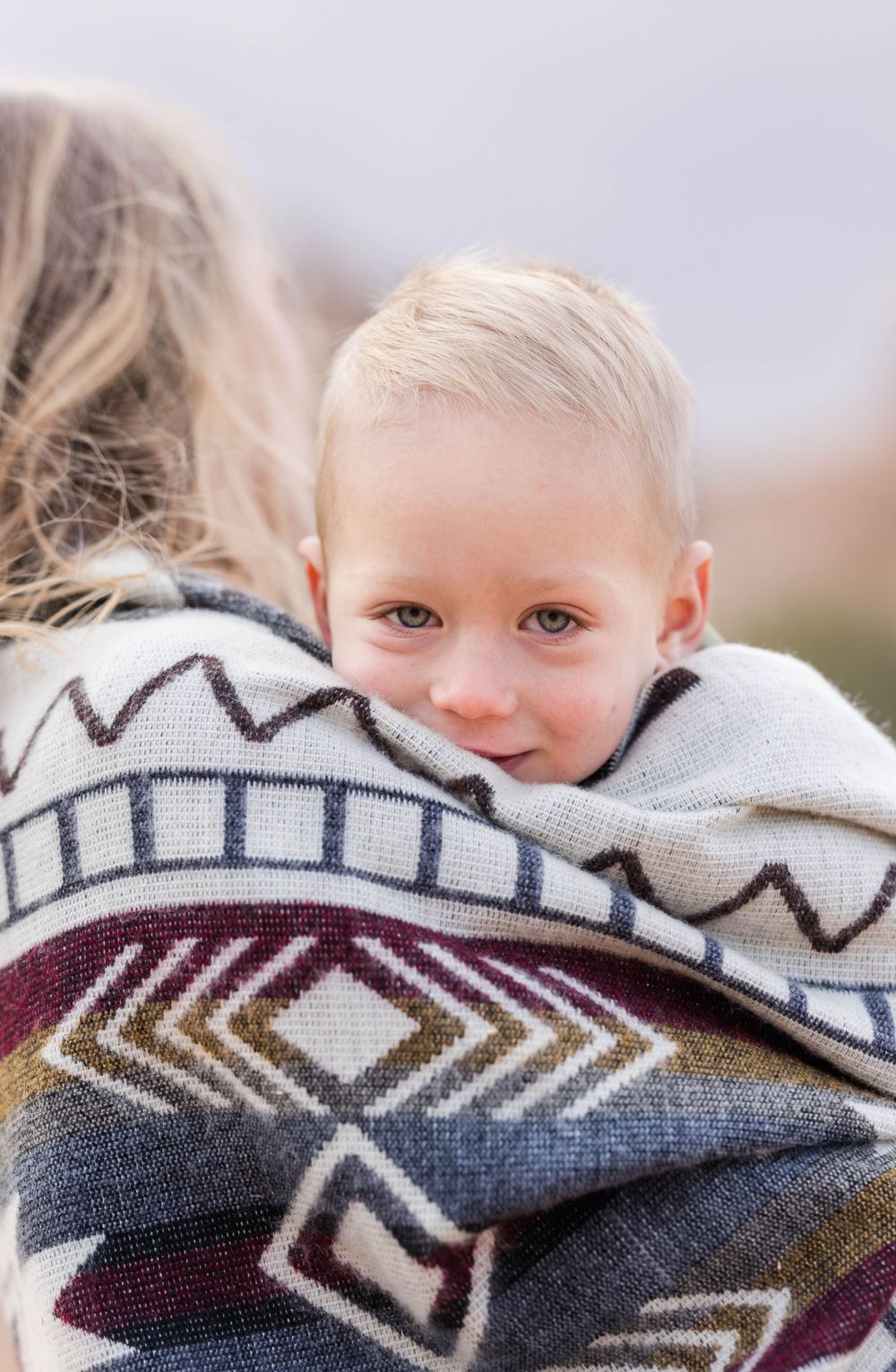 Child wrapped in tribal pattern blanket peeks over shoulder with sweet smile.