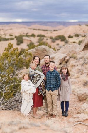 Family group poses together on rocky desert terrain with scenic canyon views.