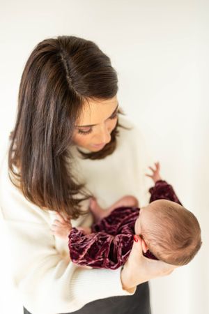 Mother in cream sweater gazes lovingly at baby wearing velvet outfit.