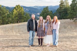 A group stands together in an open field with mountains and evergreen trees visible in the scenic background.
