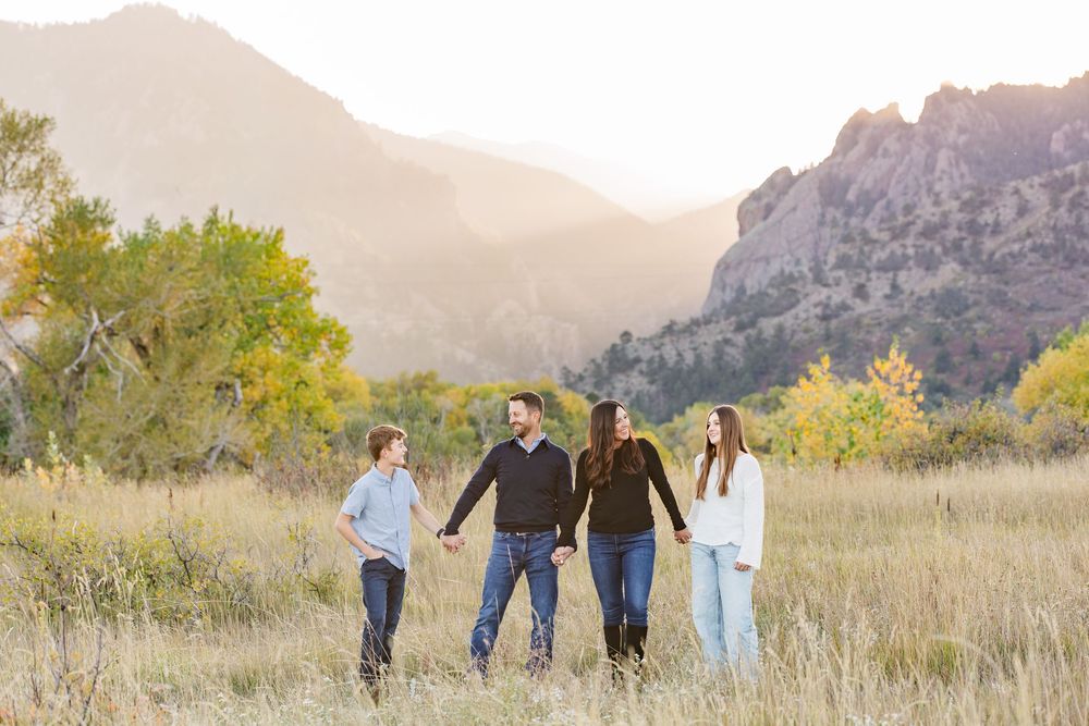 Family group walking together through golden autumn field with mountain backdrop at sunset.