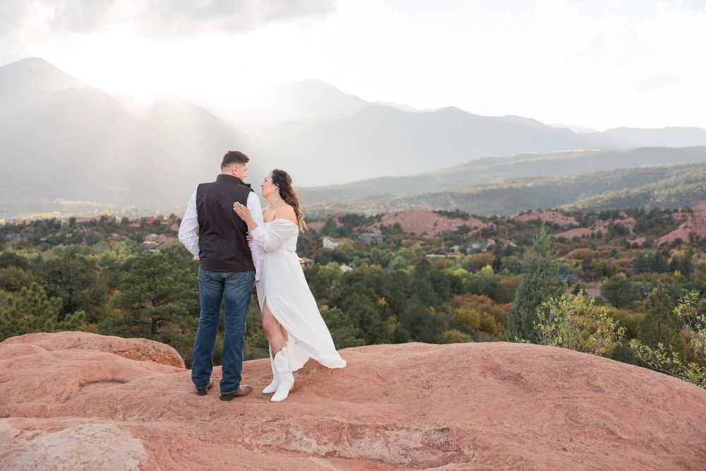 A couple stands together on red rocks overlooking Garden of the Gods park in Colorado Springs at sunset.