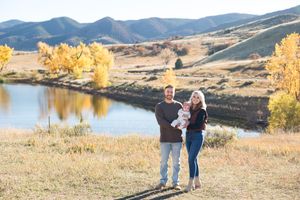 A couple walks together along a scenic mountain lake trail during golden autumn afternoon light.