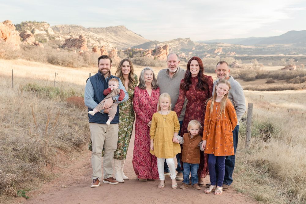 A group poses together on a hillside wearing coordinated fall-colored outfits during an autumn photo session.
