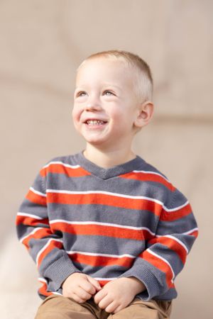 Cheerful young child wearing a striped orange and grey sweater smiling brightly.