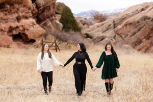 Three friends walking hand in hand through golden grass with red rock formations in the background.