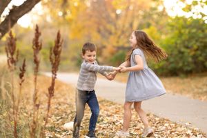 Children playing and spinning in fallen autumn leaves on a path.