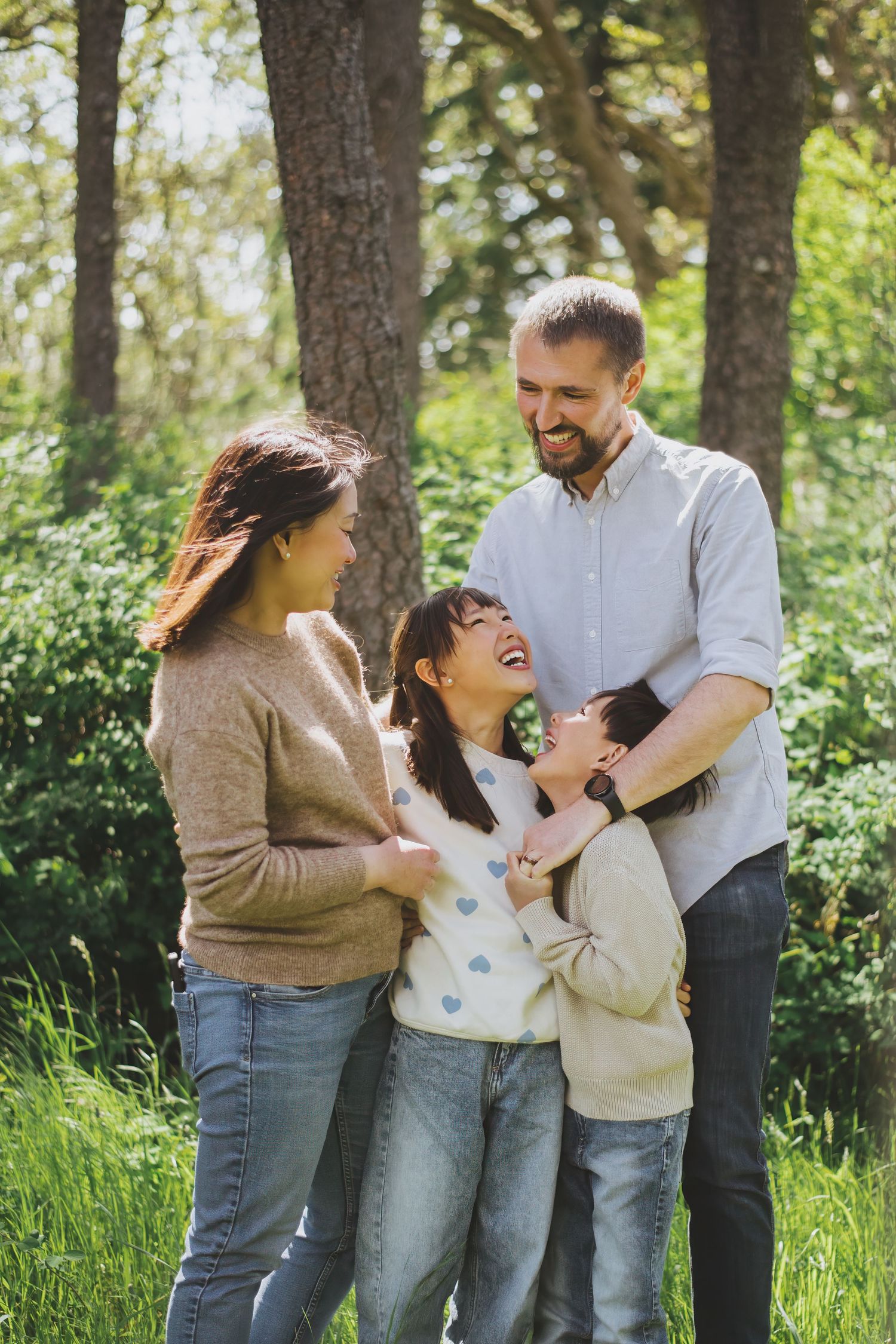 A family shares a joyful moment together outdoors in a sunlit forest setting, laughing and embracing.