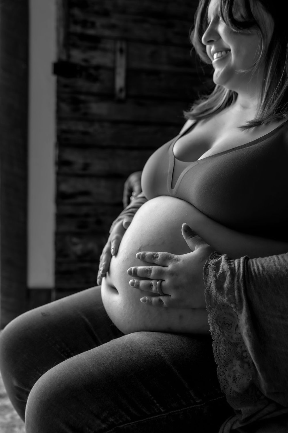 A black and white artistic maternity photo showing hands cradling a pregnant belly against a dark background.
