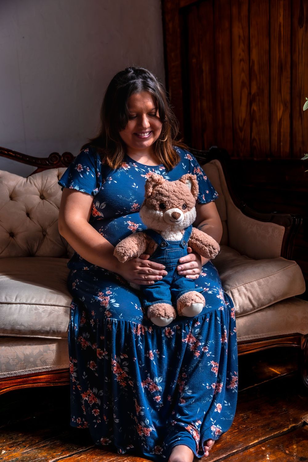 Someone wearing a blue floral dress sits on a beige couch holding a matching teddy bear in identical outfits.