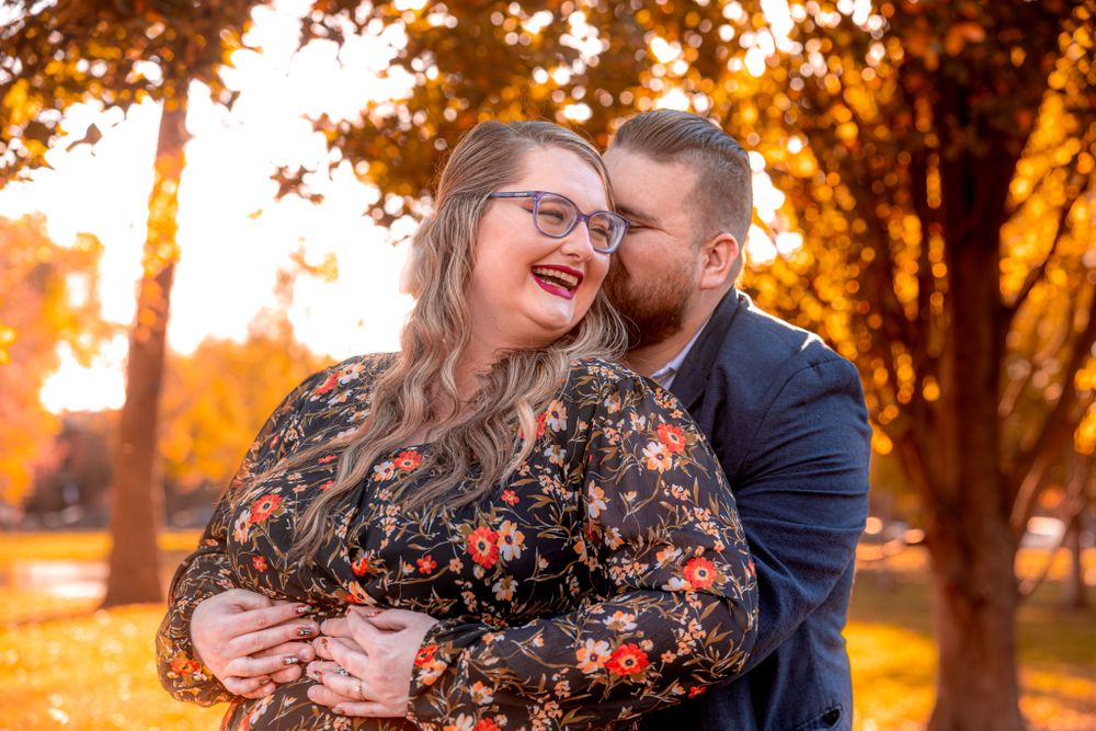 Joyful couple embraces in a park during golden hour sunset with autumn trees glowing in the background.