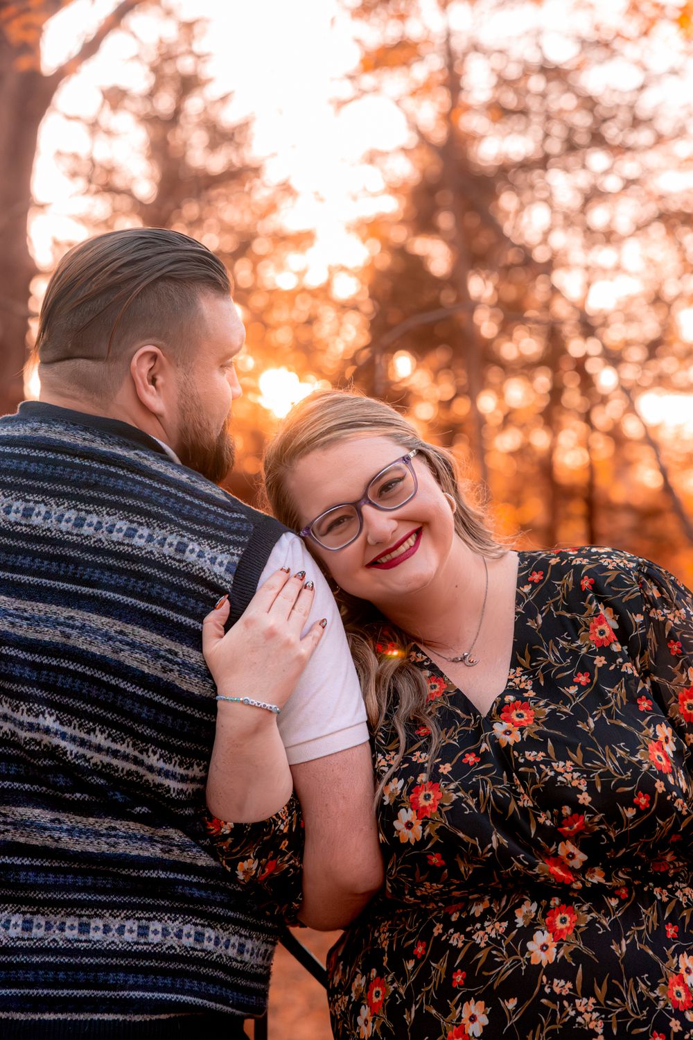 A couple shares an intimate moment during sunset, with the woman wearing a floral dress and smiling warmly.