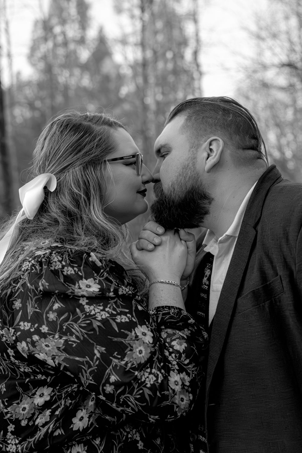 A romantic black and white portrait of a couple sharing an intimate moment outdoors with trees in the background.