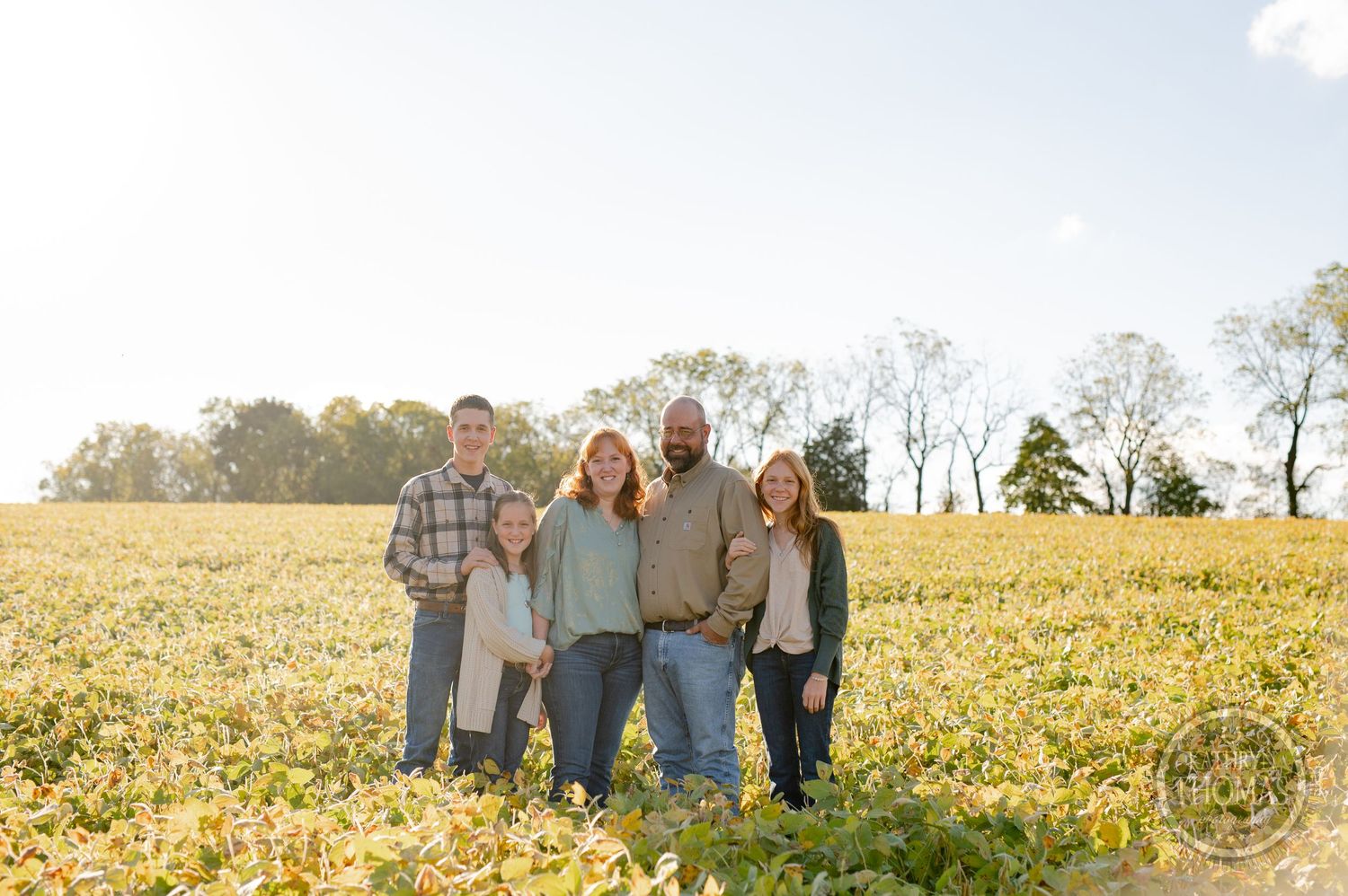 Family of five poses together in a sunny autumn field with golden flowers.