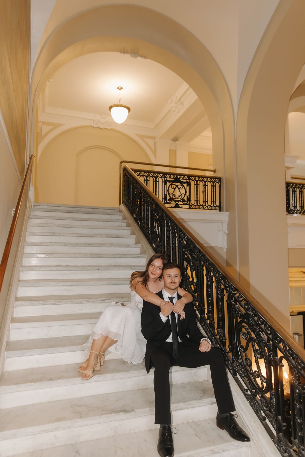 A series of wedding photos showing a couple posing on an elegant white marble staircase with ornate black railings.