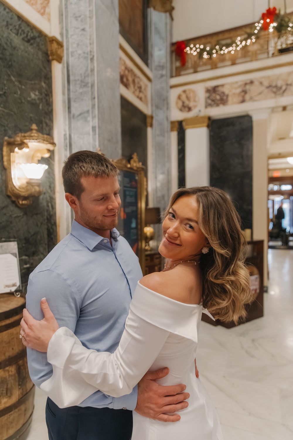 A couple shares romantic moments in an elegant marble-columned venue with sparkling lights and ornate decor.