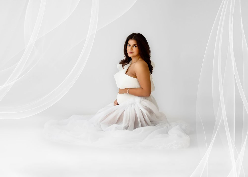 Graceful maternity portrait with billowing white fabric in dreamy studio setting.