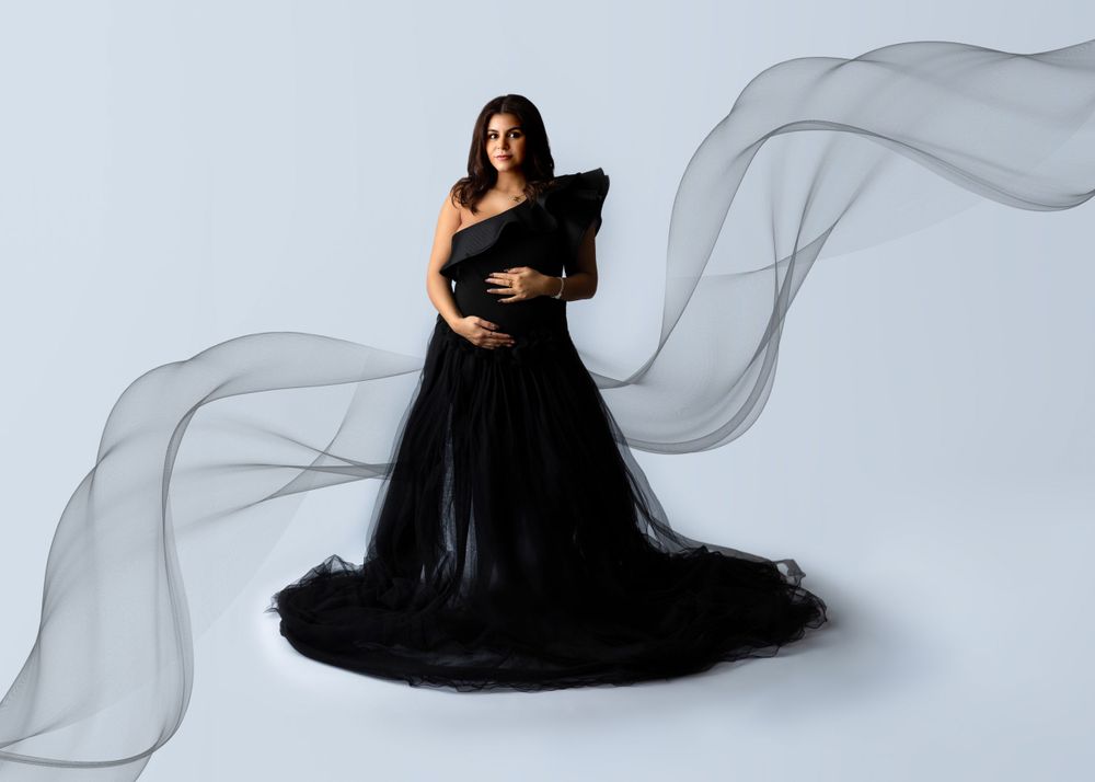 Dramatic maternity portrait in black gown with flowing fabric against white background.
