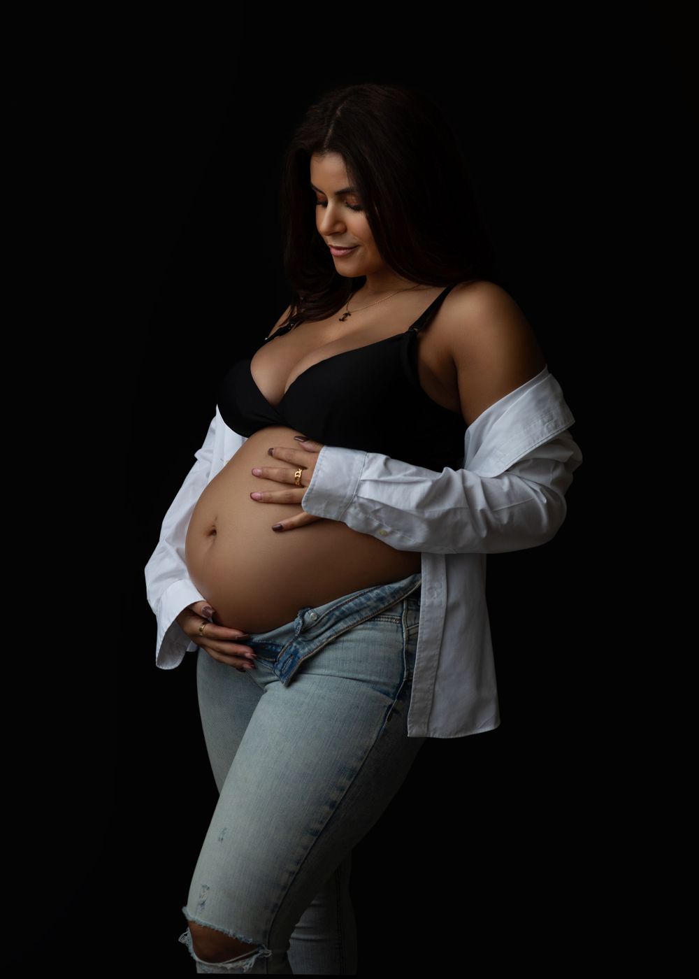 Artistic maternity photo with woman in black top and jeans with white button-down shirt.