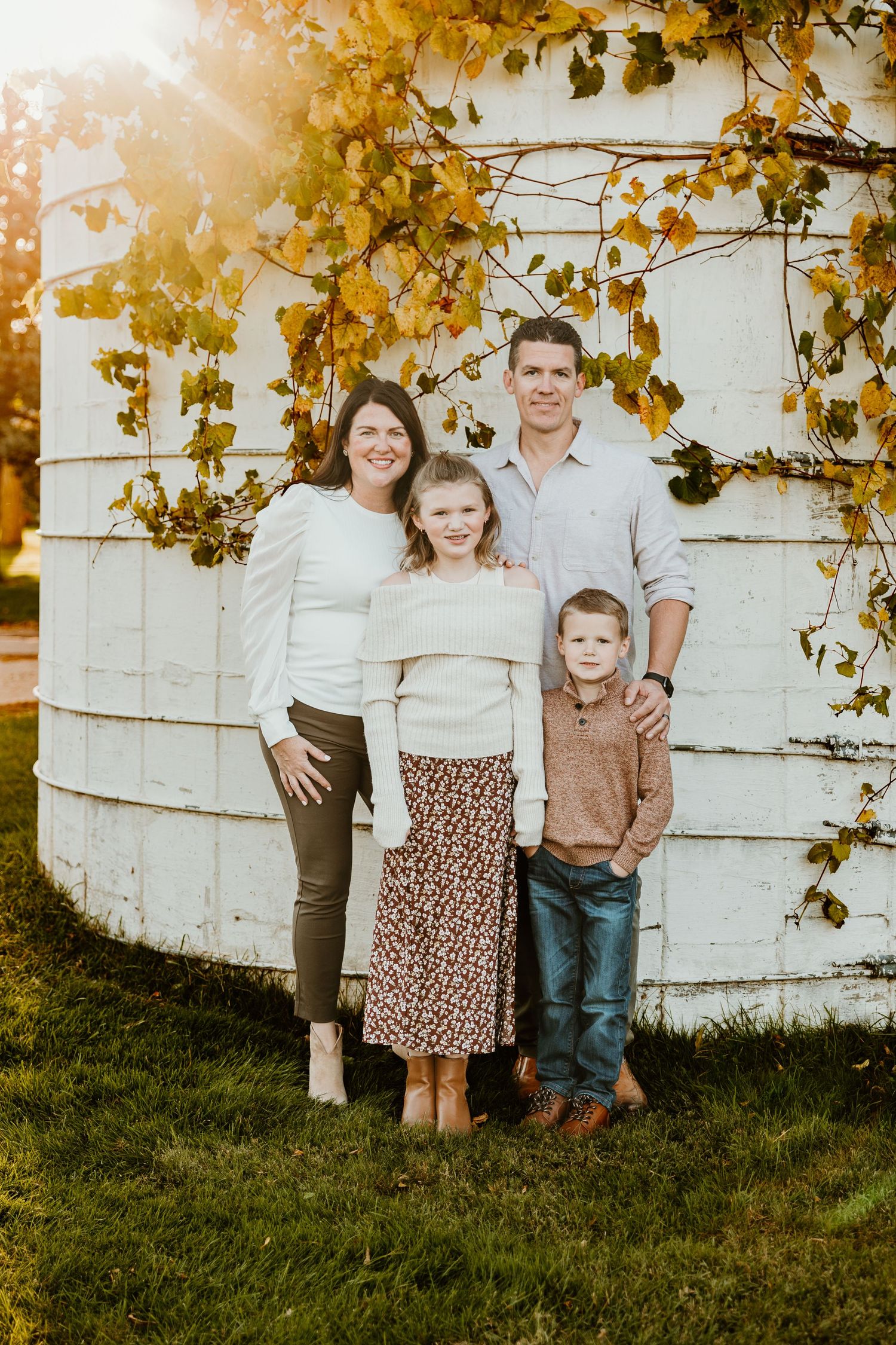 Family poses together against white silo with autumn vines during sunset in Livonia Michigan at Greenmead Historical Park.