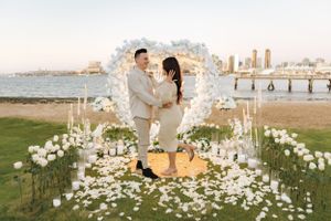 Beautiful proposal setting with white flower arch, candles and scattered petals overlooking waterfront.