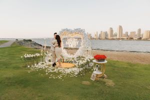 Seaside proposal setup with floral arch, decorative elements and city skyline view.