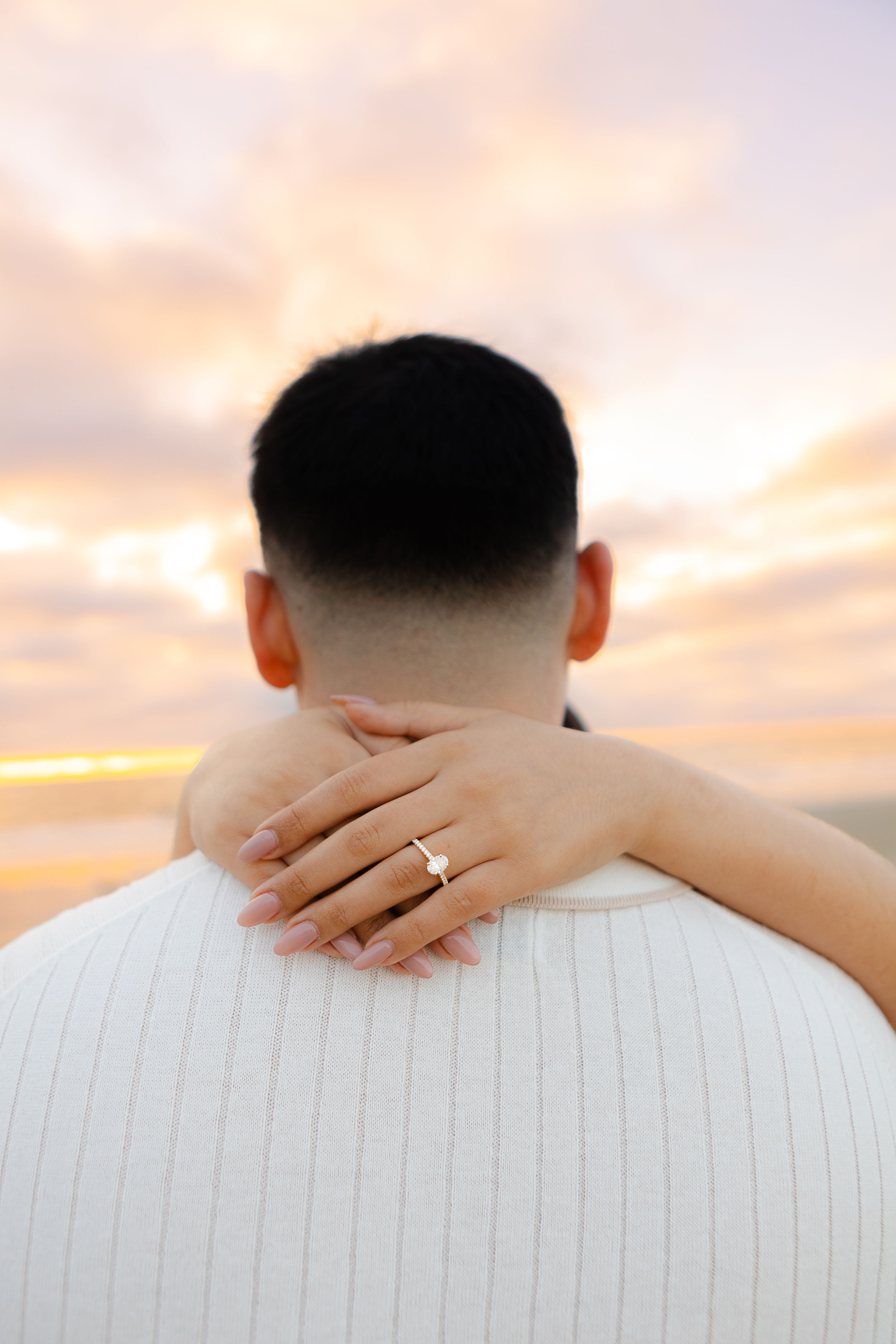 Close-up of engagement ring display with sunset beach backdrop.