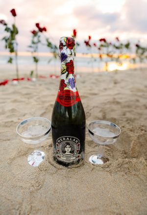 Champagne bottle and glasses set up on beach sand with red roses at sunset.