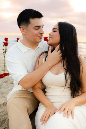Intimate beach portrait with red roses and golden sunset lighting.