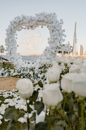 White floral arch with illuminated proposal sign against city skyline at dusk.
