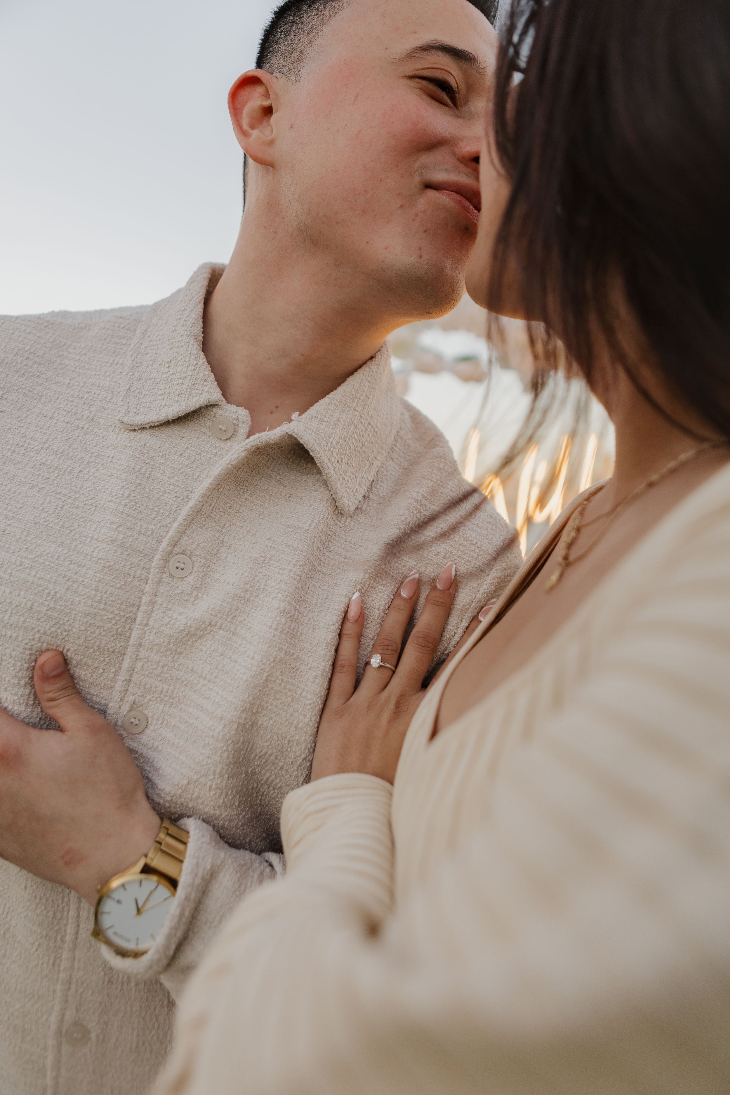 Intimate engagement portrait showing ring and light cream colored outfits at sunset.