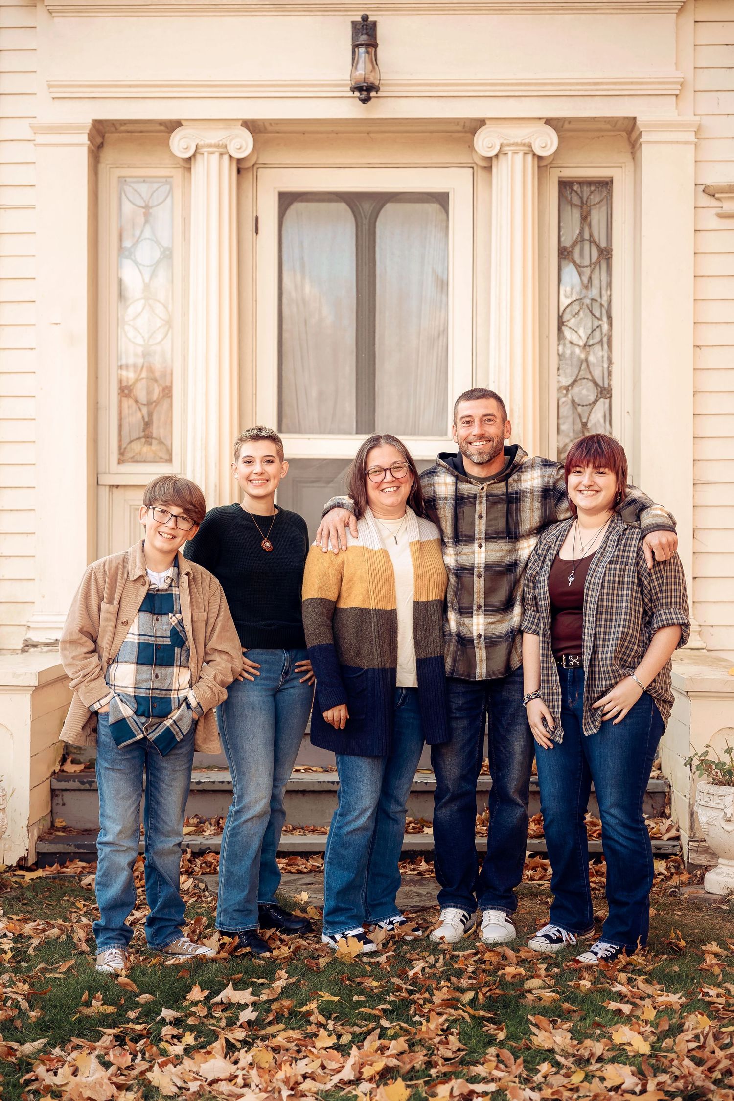A family poses together on the front steps of a cream-colored historic building. Michigan Detroit Novi Northville Portrait Photographer