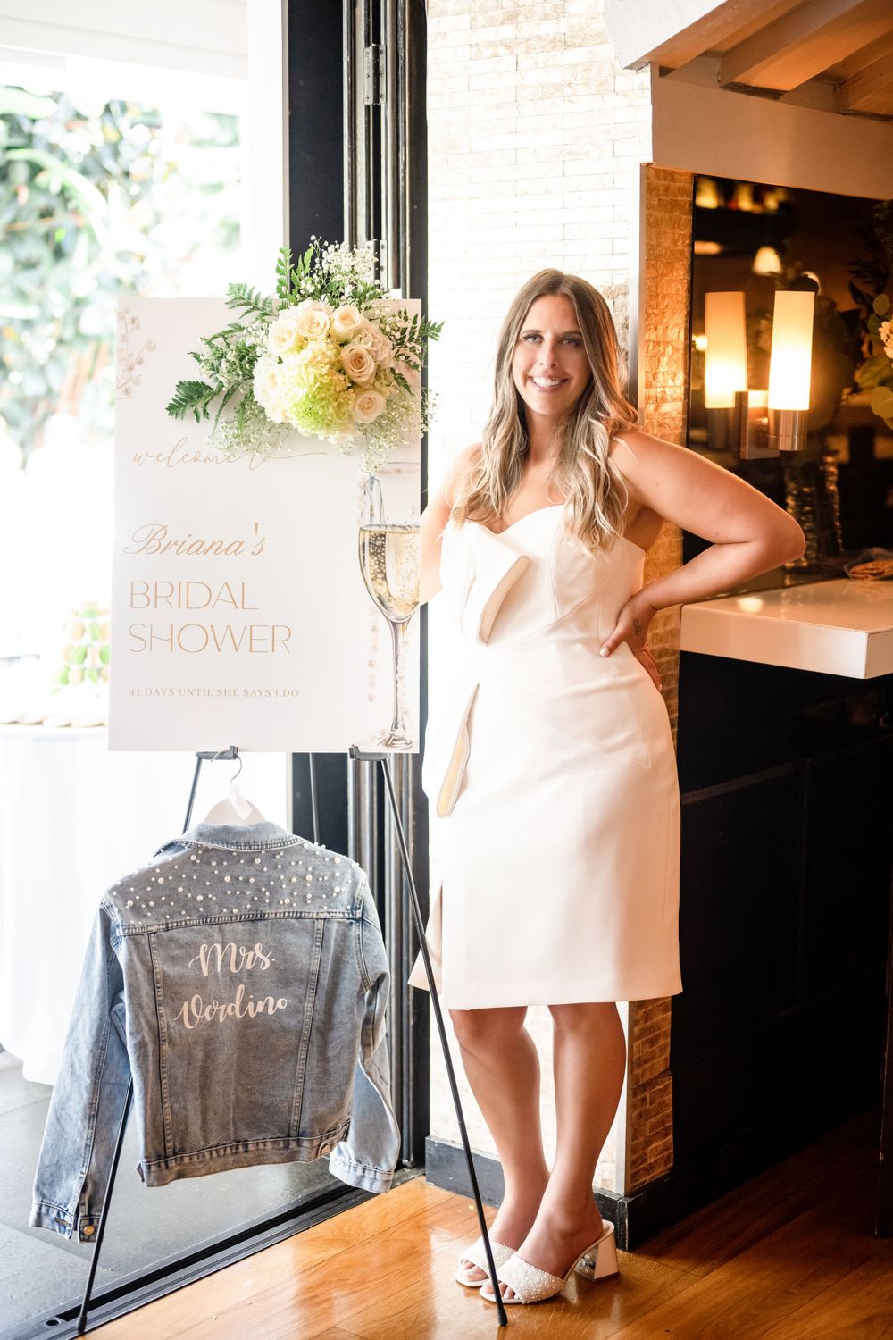 Bridal shower setup with white dress, floral arrangements and customized denim jacket decor.