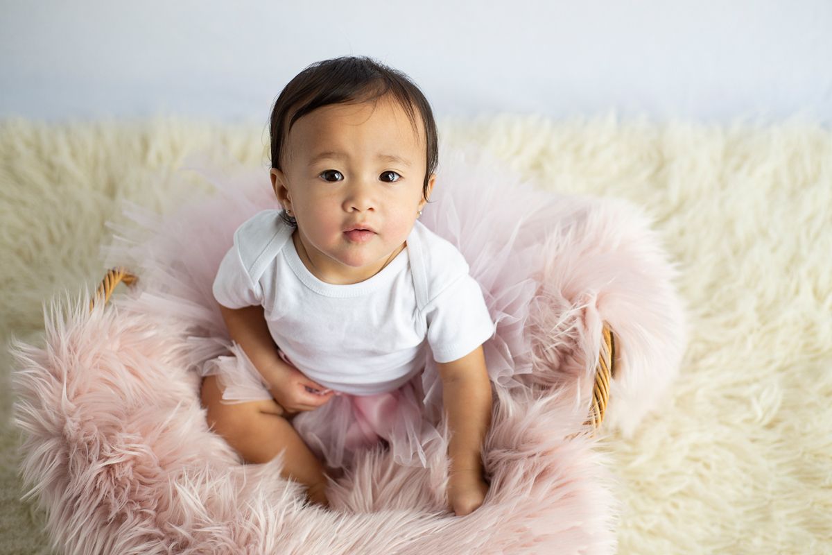 little girl sits up in basket with pink fur looking up at camera