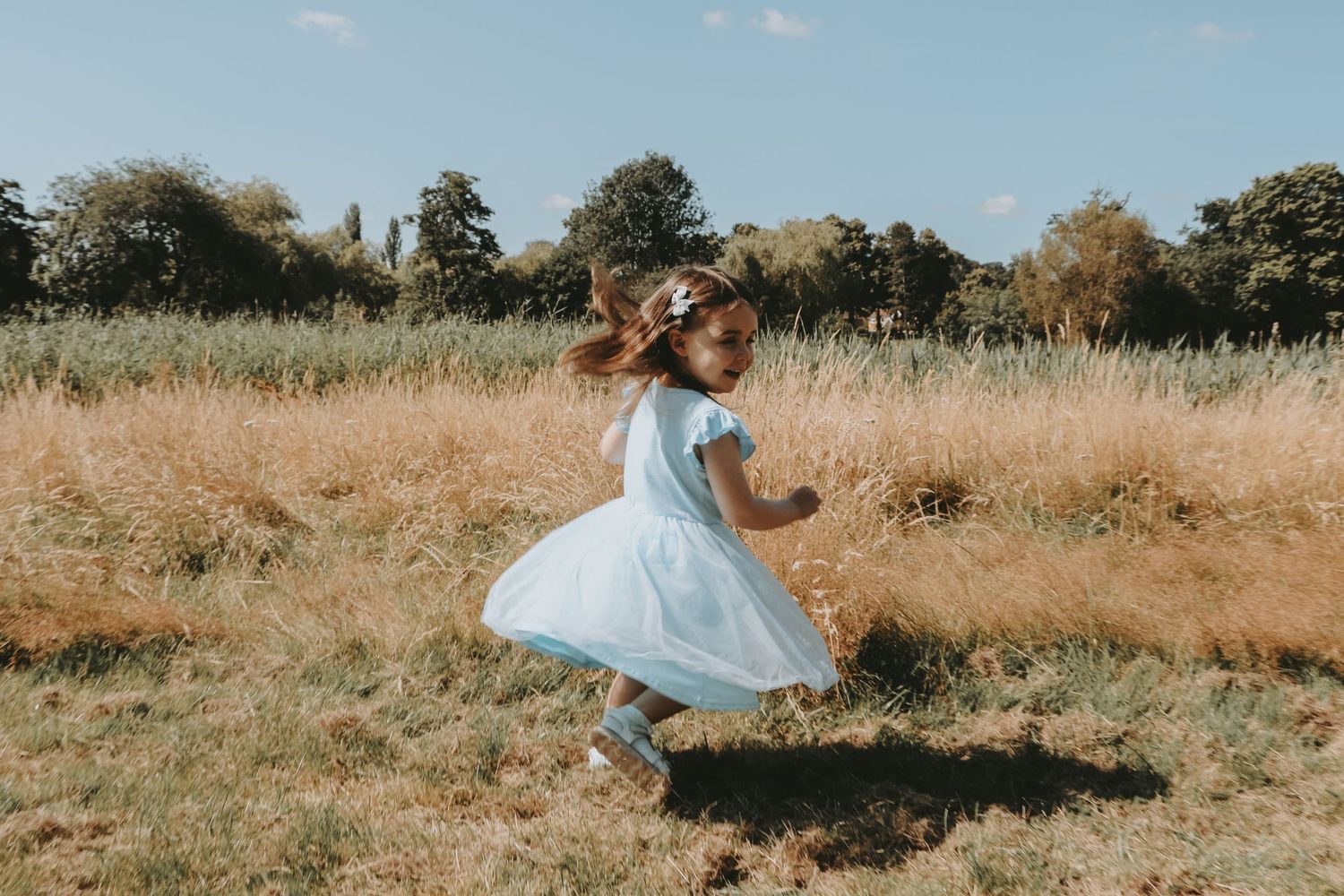 Young person in light blue dress twirling in a sunny meadow.