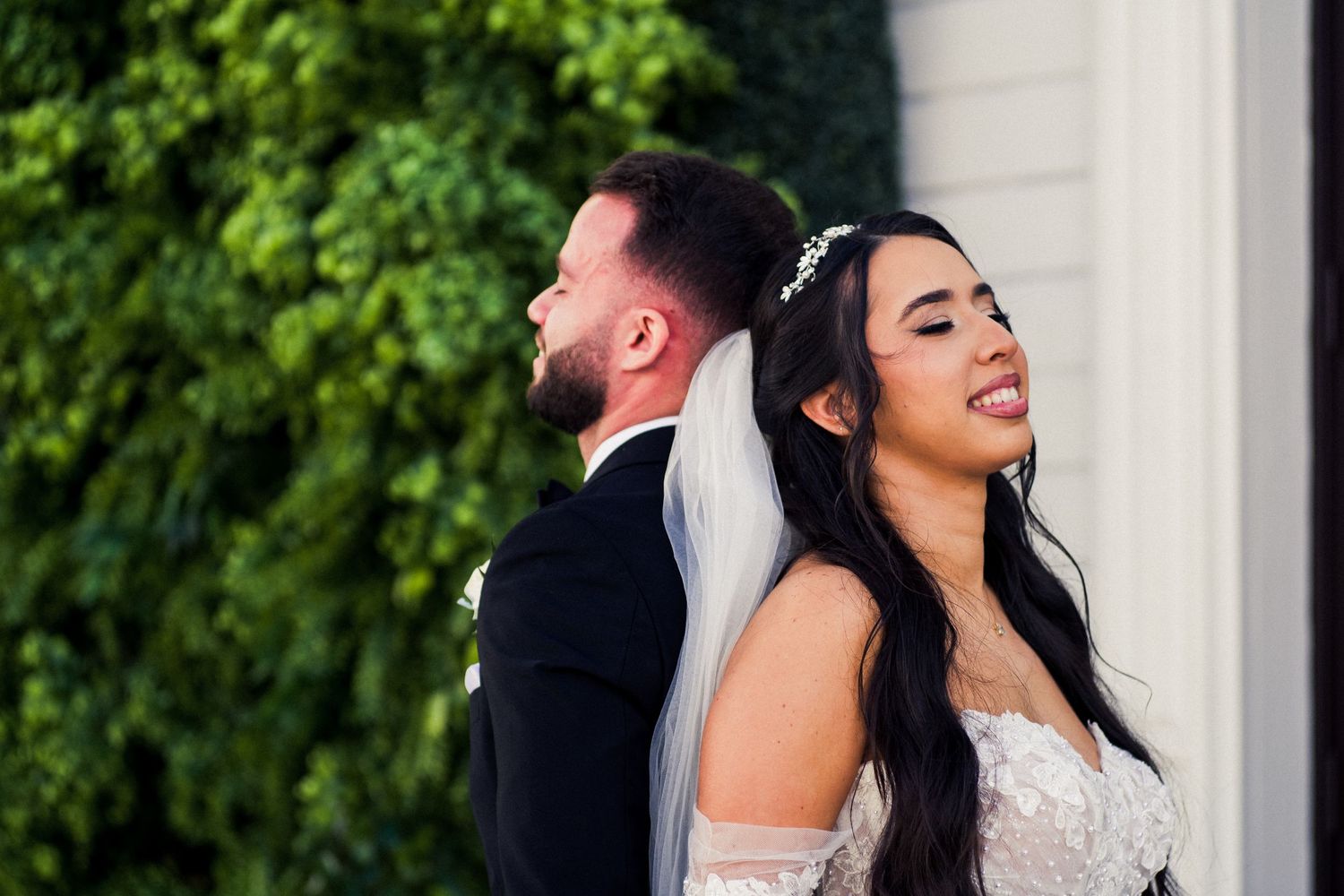 A candid wedding portrait against a lush green backdrop with natural lighting.