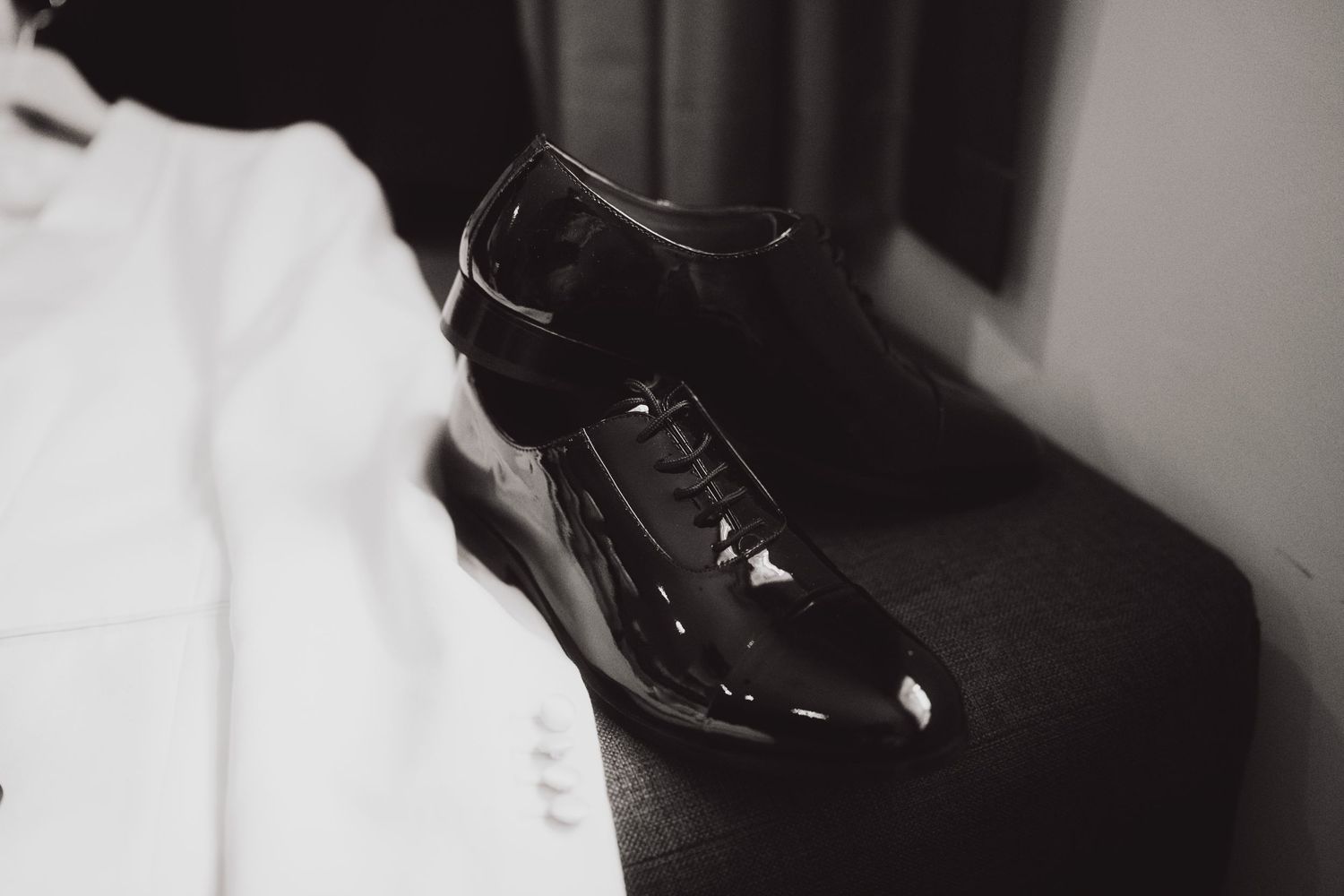 Close-up shot of a shiny black patent leather formal dress shoe against a white background.